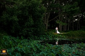 At 1812 Farm in Bristol, Maine, the bride and groom embrace on the opposite side of a pond, their reflection visible in a small opening among the lily pads.